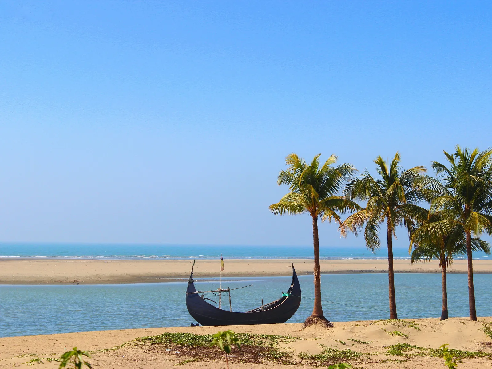 Palms and a fishing boat on turquoise water at Cox's Bazar